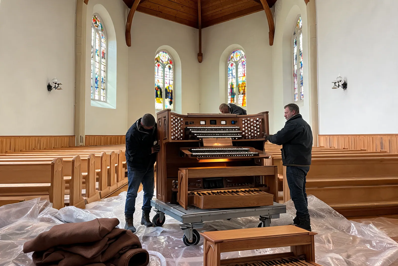 To personer flytter en orgelkonsoll inne i en kirke